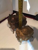 Two vintage brass jewelry boxes with embossed vines and swirls shown side by side with measuring tape for scale