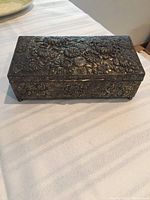 Closed view of brass floral embossed rectangular box showing top and front side with detailed floral patterns.