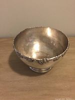 Silver rose bowl with detailed grape and vine pattern on rim, showing some antique wear and scratches.