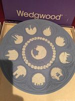 Photo of a circular light blue Wedgwood jasperware plate with white relief silhouettes arranged in a ring with a decorative leaf and rope border