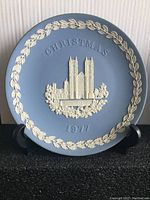 Front view of Wedgwood Christmas plate from 1977 with white relief design of Westminster Abbey and leaf border on light blue background.