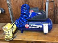 Full view of Campbell Hausfeld air compressor with attached blue and yellow coiled hoses on a wooden surface.