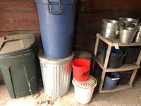 Photo shows multiple garbage cans stacked including a green plastic can, blue plastic can, silver metal can, a small white metal can with a lid, and a red plastic bucket on top