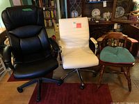 Photo shows the three chairs: black padded leather-like office chair, white ribbed office chair with chrome armrests, and wooden chair with blue cushion