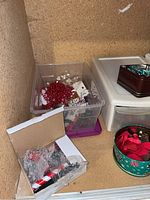 Clear plastic container with red bead garlands, white and silver bead garlands, small Christmas ornaments, and green glass candle holders