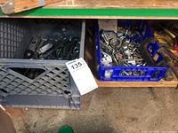 Photo showing two crates used for storage: one gray plastic crate containing socket wrenches and similar tools, the other blue crate with assorted nuts and small metal hardware.