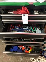 Metal drawer open showing multiple screwdrivers, pliers with blue and green handles, and other small hand tools in a metal tool cabinet drawer with a Black & Decker wrench set sticker visible on bottom drawer front.