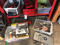View showing two plastic bins, one with assorted hardware including clamps and tools, and one with heat gun in box and other items.