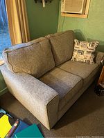 Side view of grey fabric love seat showing wide padded armrest and part of decorative pillow.