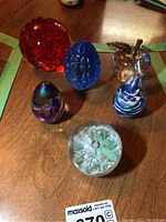 Six glass paperweights displayed on wooden table showing various shapes, colors, and textures.