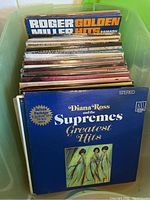 Top view of a green bin containing multiple vinyl records, frontmost is 'Diana Ross and the Supremes Greatest Hits' album with deep blue cover and gold lettering.