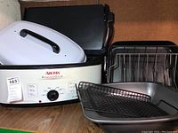Photo showing Aroma Roaster Oven with several trays and racks placed in front, white lid with black handle, metal racks and baking trays of different sizes