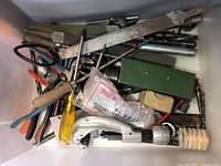 Top view showing assorted hand tools including screwdrivers, pipe cutter, pliers, nails, files, and rusted saw blade.