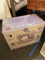 Photo of Singer Simple 3232 sewing machine box showing branding, machine image, and features on the side panel.