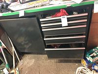 Front view of black Craftsman tool cabinet showing multiple drawers and side cabinet door open with shelving inside, stored in garage.