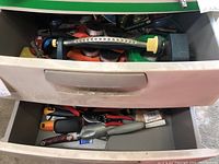 Another drawer containing hand tools such as pruners, a metal trowel, and small shrub shears.