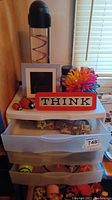 Full view of the vintage IBM THINK sign on top of white plastic drawers containing toys and collectibles including colorful figurines and plastic containers.