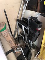 View of folded Carex wheelchair with attached black nylon storage pouch, cardboard box with ramp inside, and leaning crutches in corner.