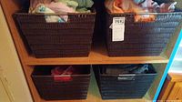 Four brown wicker baskets on wooden shelves filled with assorted women's clothing items in various colors and sizes.