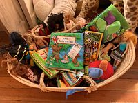 Woven basket containing several Barbie dolls in various outfits and multiple fabric books including 'Owl Saves The Day'
