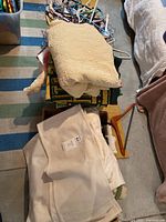 Folded blankets and a basket stacked together on the floor over a striped rug with some hangers underneath.
