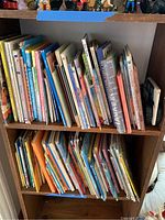 Two shelves packed with children's books spaced vertically and placed tightly side by side on wooden shelving unit.