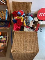 Basket containing kids jackets, gloves and umbrellas in a basement setting near a stop sign and bookshelves.