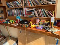 Full shelf with various collectible toys, figurines, masks, and Mickey Mouse items displayed beneath a bookshelf filled with books