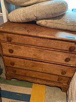 Front view of the four drawer wooden dresser with cushions on top, showing overall condition and finish.