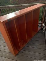 Orange painted metal shelf unit showing full view with multiple vertical compartments and slotted base