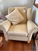 Front view of creamy yellow upholstered rocking chair with matching pillow placed on seat. Shows armrests and wooden rocking legs.
