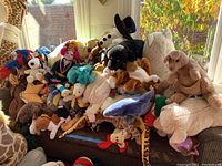 Photo showing many stuffed animals and toys piled on a couch including a giraffe neck, bears, doll, Batman, shark, and other animals.