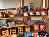 Full view of vintage toys, art supplies, and bins arranged on a wooden shelf and table. Includes toy telephones, binoculars, shape sorters, and piggy banks.