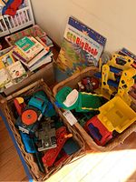 Photo showing wicker baskets filled with colorful plastic toy vehicles including dump trucks, tractors, and a collection of children's books.