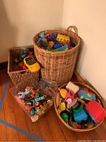 Photo showing three containers: two woven baskets and one clear plastic bin filled with various toys including blocks, cars, and animal figurines.