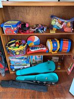Shelf display of assorted toy drums, puzzles, toy tambourine, xylophone, building blocks, and cases for toys or instruments.