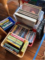 Wide shot of multiple containers filled with vinyl records, DVDs, and CDs on a wooden floor