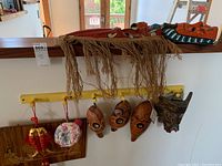 Seven tribal masks displayed; one large red with fringe and six smaller variously colored hanging masks