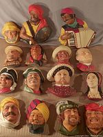 Full collection laid out showing 15 colorful chalkware busts in various costumes and headwear with detailed facial features.