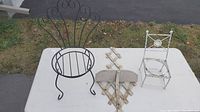 Top view of large black metal chair-shaped plant holder with ornate scrollwork backrest and circular seat base, placed on white table outdoors