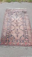 Full view of the antique rug laid out on pavement showing overall design and wear.