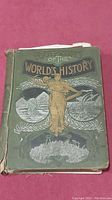 Front cover of the book showing green cloth with gold and dark printed illustrations and title.