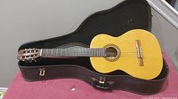 Acoustic guitar inside an open black hard case, showing the full body of the guitar