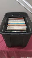 Black plastic container filled with over 110 LP records stored vertically showing spines.
