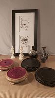 Full lot showing two framed dog prints, two white classical female figurines, two purple wooden plant stands with gold trim, two black carved wooden plant stands, and three decorative vases.