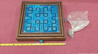 Top view of the square maze game with wooden frame and blue plastic maze with numbered paths and knobs on the sides