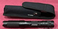 Laser pointer and carrying case laid out on red surface