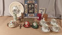 Wide view of whole collection showing framed bird picture, porcelain plate, tea cups, scissors, small vase, small carved figure, and cylindrical containers.