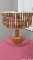 Front angled view of midcentury teak wood tri-light table lamp on a red surface, showing wooden slat shade and cylindrical wood base