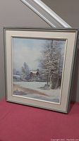 Framed oil painting showing winter landscape with snow-covered trees and buildings.